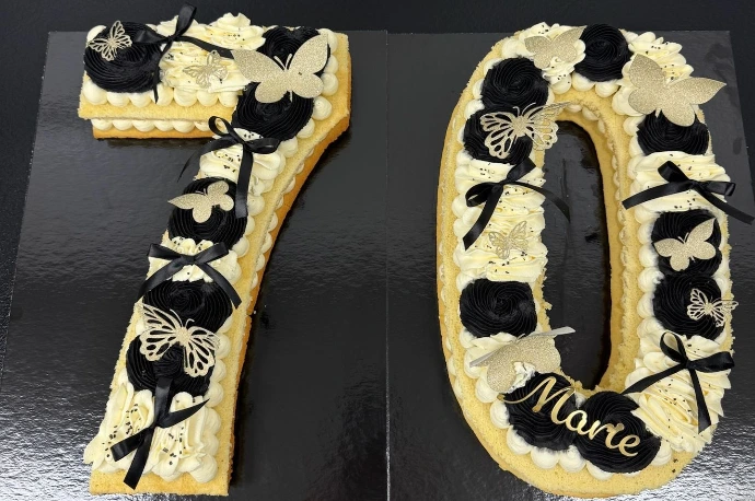 Gâteau chiffre 70 noir et doré décoré de rubans et de gourmandises.